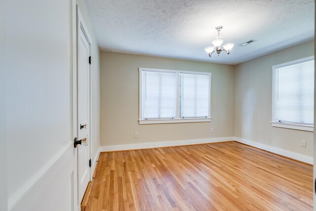 spare room with light hardwood / wood-style flooring, a chandelier, a textured ceiling, and a healthy amount of sunlight