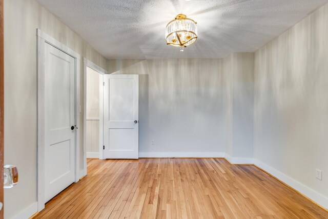 spare room featuring an inviting chandelier, a textured ceiling, and light hardwood / wood-style flooring