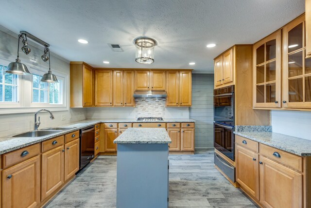 kitchen featuring light stone countertops, light wood-type flooring, a center island, and sink