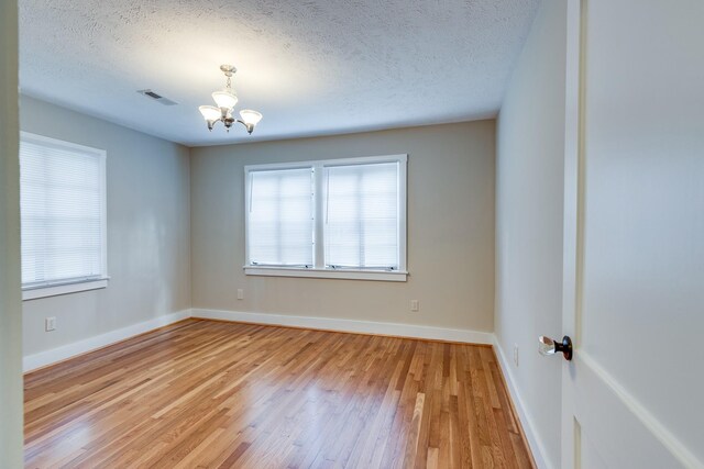 spare room with an inviting chandelier, a textured ceiling, and light hardwood / wood-style flooring