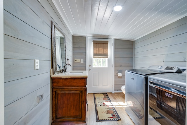 laundry area with independent washer and dryer, wood walls, light wood-type flooring, wooden ceiling, and sink