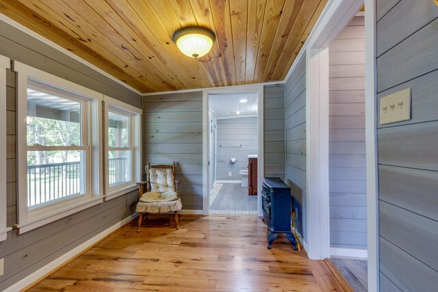 living area with lofted ceiling, wood walls, a wood stove, light hardwood / wood-style flooring, and wooden ceiling