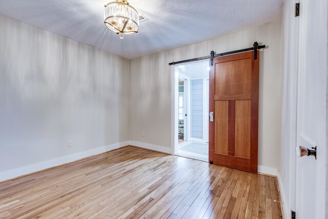 empty room featuring a textured ceiling, light wood-type flooring, a chandelier, and a barn door