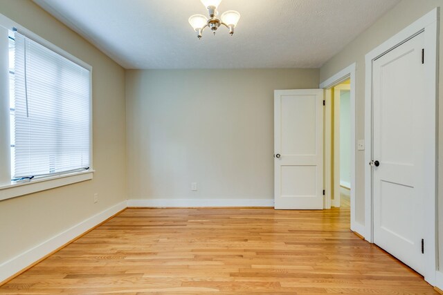 empty room with light wood-type flooring, a chandelier, a textured ceiling, and plenty of natural light