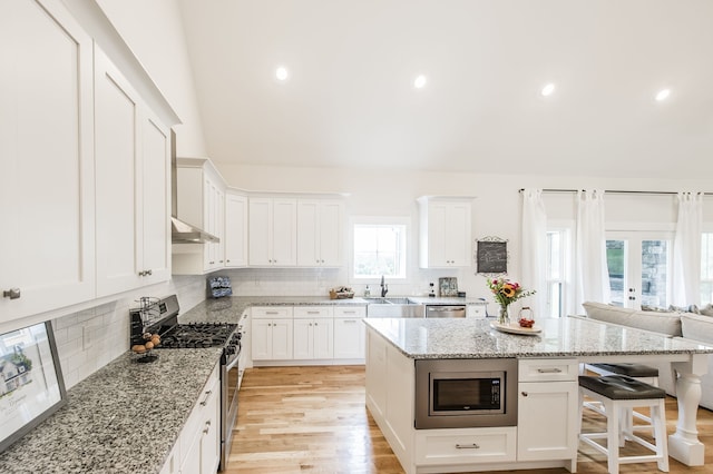 kitchen featuring appliances with stainless steel finishes, white cabinetry, light stone countertops, light wood-type flooring, and a center island