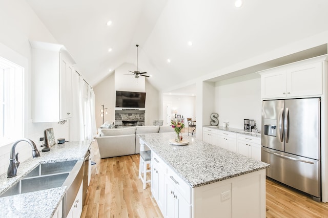 kitchen featuring ceiling fan, light wood-type flooring, stainless steel refrigerator with ice dispenser, a fireplace, and vaulted ceiling