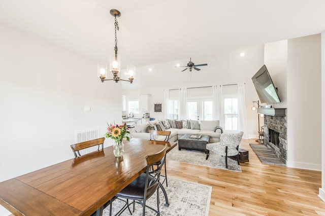 dining area featuring ceiling fan with notable chandelier, light wood-type flooring, a fireplace, and sink