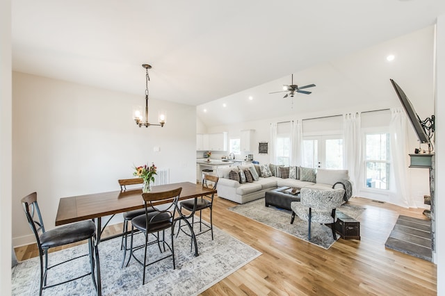 dining area with ceiling fan with notable chandelier, light wood-type flooring, and vaulted ceiling