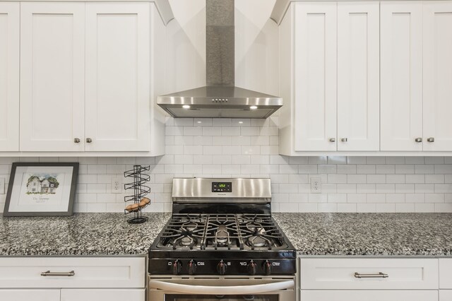 kitchen with wall chimney exhaust hood, white cabinetry, stainless steel gas range oven, and stone countertops