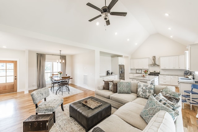 living room featuring ceiling fan with notable chandelier, sink, high vaulted ceiling, and light hardwood / wood-style flooring