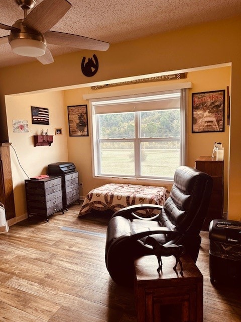 living area with ceiling fan, a textured ceiling, and light wood-type flooring