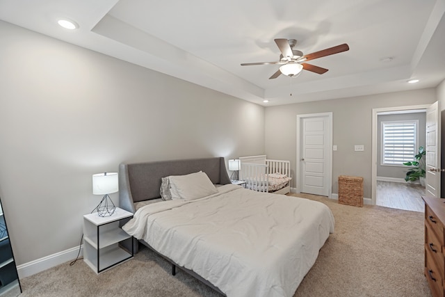 bedroom featuring ceiling fan, light colored carpet, and a tray ceiling