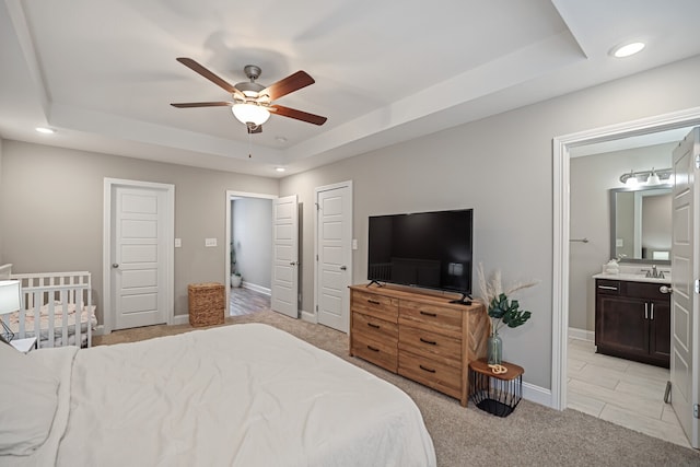 carpeted bedroom with ceiling fan, a raised ceiling, connected bathroom, and sink