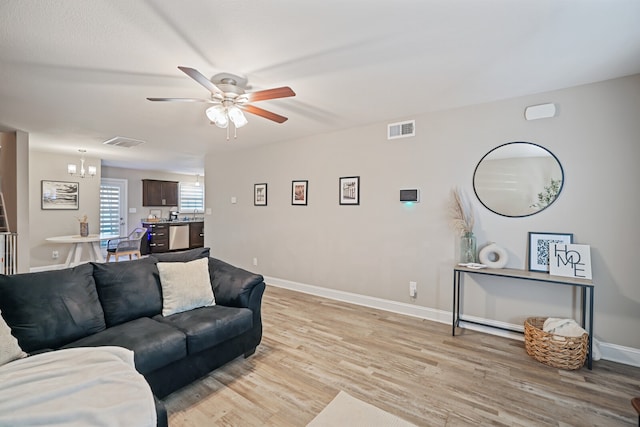 living room with ceiling fan with notable chandelier and light hardwood / wood-style flooring