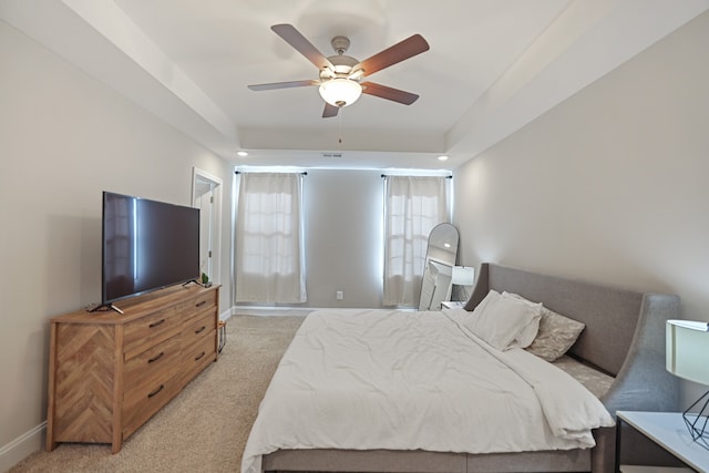 bedroom featuring ceiling fan, light colored carpet, and a tray ceiling