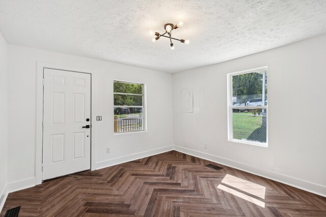 spare room with a wealth of natural light, a textured ceiling, and dark parquet flooring