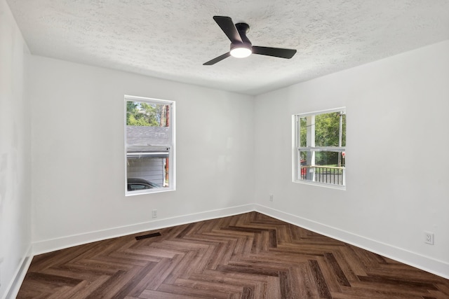 empty room featuring ceiling fan, dark parquet flooring, and a wealth of natural light