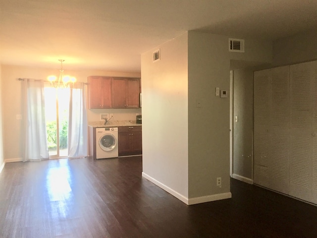 unfurnished living room featuring dark wood-type flooring, washer / dryer, and an inviting chandelier