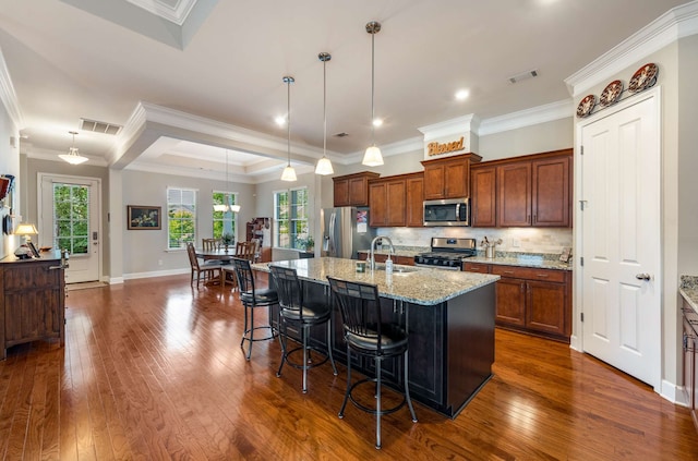 kitchen featuring a kitchen breakfast bar, dark wood-type flooring, stainless steel appliances, decorative light fixtures, and a center island with sink