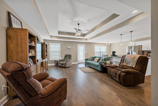 living room with a textured ceiling, a raised ceiling, dark hardwood / wood-style flooring, and ceiling fan