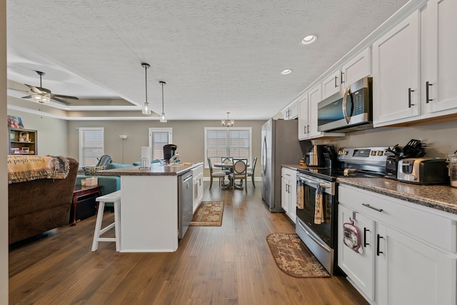 kitchen with appliances with stainless steel finishes, hanging light fixtures, white cabinetry, a kitchen island, and ceiling fan