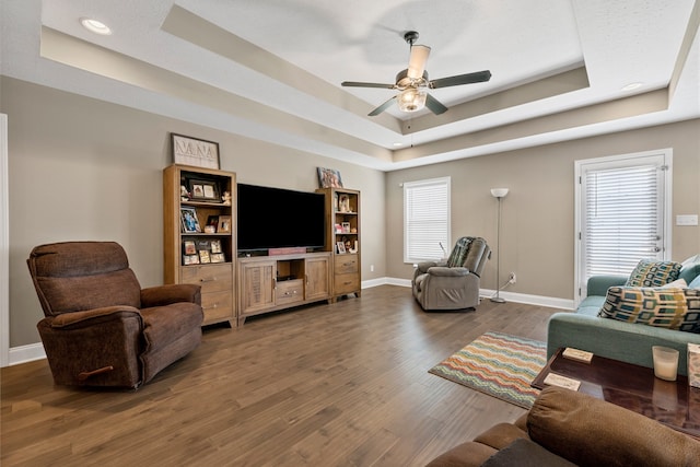 living room featuring ceiling fan, a raised ceiling, and dark wood-type flooring