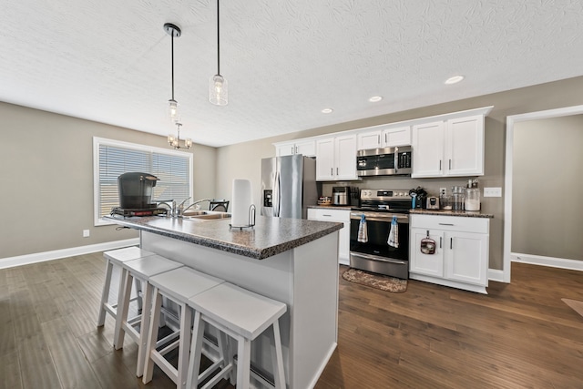 kitchen with white cabinets, pendant lighting, dark wood-type flooring, appliances with stainless steel finishes, and a breakfast bar area