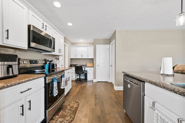 kitchen featuring built in desk, white cabinetry, stainless steel appliances, wood-type flooring, and decorative light fixtures