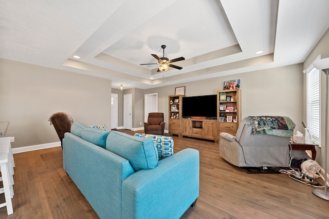 living room featuring ceiling fan, a raised ceiling, and wood-type flooring