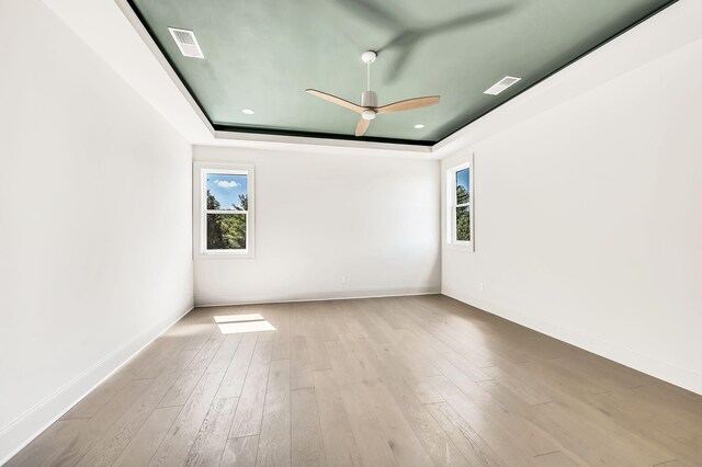 spare room featuring ceiling fan, a healthy amount of sunlight, a raised ceiling, and light hardwood / wood-style flooring