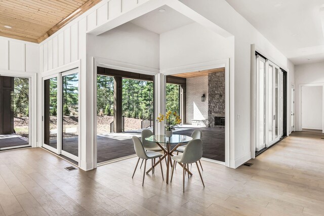 interior space featuring a stone fireplace, a towering ceiling, wood ceiling, and light hardwood / wood-style flooring