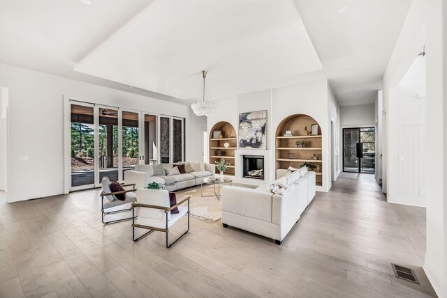 living room with built in shelves, an inviting chandelier, and light wood-type flooring