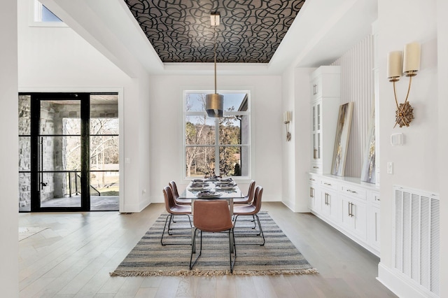 dining space featuring light hardwood / wood-style flooring, a raised ceiling, and a healthy amount of sunlight