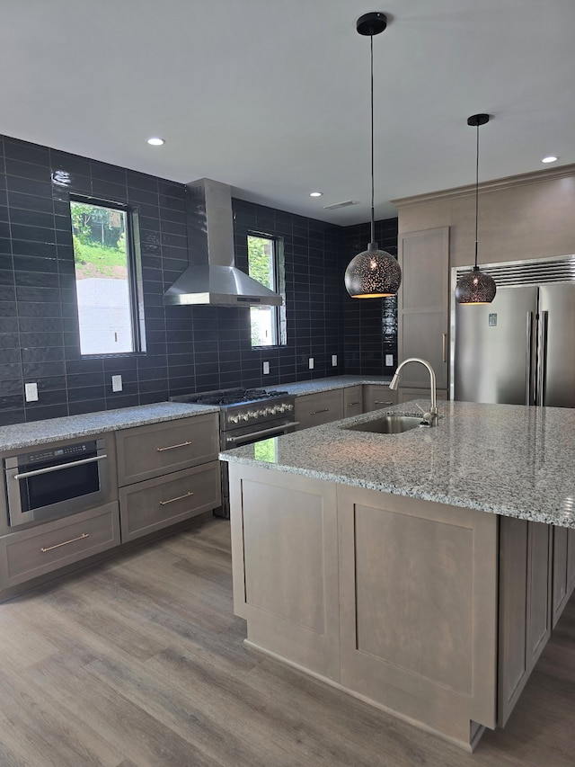 kitchen with wall chimney exhaust hood, light stone countertops, pendant lighting, wood-type flooring, and sink