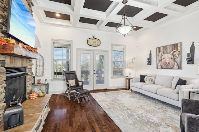 living room with beamed ceiling, wood-type flooring, a stone fireplace, french doors, and coffered ceiling