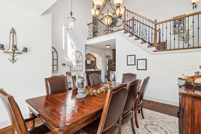 dining space with an inviting chandelier, wood-type flooring, and a towering ceiling