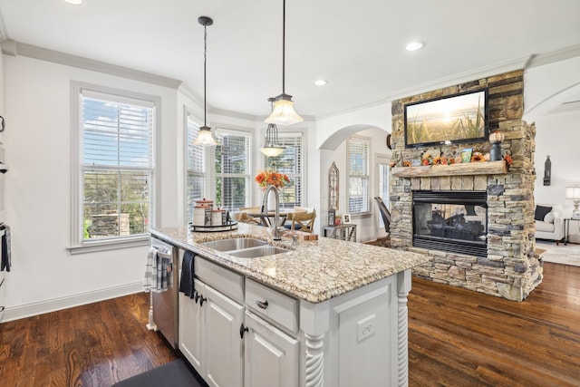 kitchen with pendant lighting, sink, a stone fireplace, a center island with sink, and white cabinetry