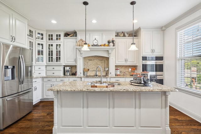 kitchen featuring appliances with stainless steel finishes, hanging light fixtures, white cabinets, a center island with sink, and sink