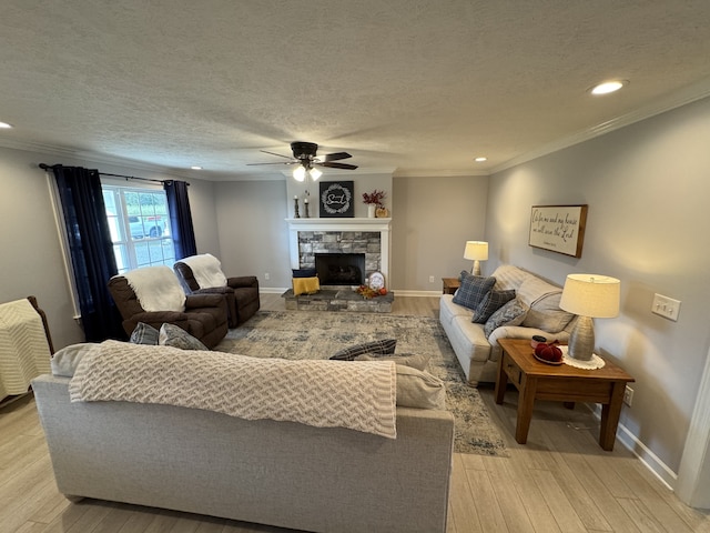 living room featuring ceiling fan, a textured ceiling, light hardwood / wood-style flooring, a fireplace, and crown molding