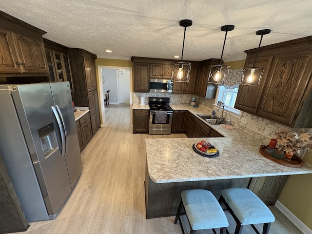 kitchen with hanging light fixtures, sink, kitchen peninsula, appliances with stainless steel finishes, and light hardwood / wood-style floors