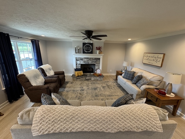 living room featuring a stone fireplace, crown molding, light hardwood / wood-style floors, and ceiling fan