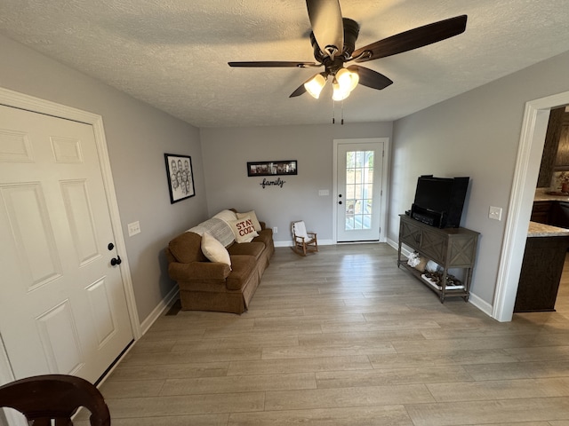 living room with light wood-type flooring, ceiling fan, and a textured ceiling