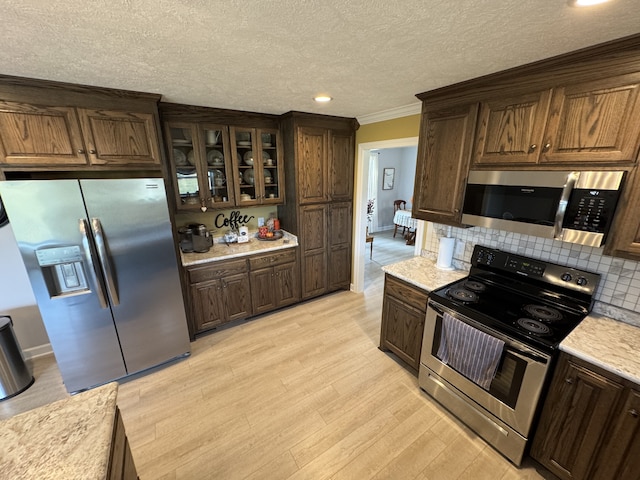 kitchen with appliances with stainless steel finishes, light hardwood / wood-style floors, backsplash, light stone countertops, and ornamental molding