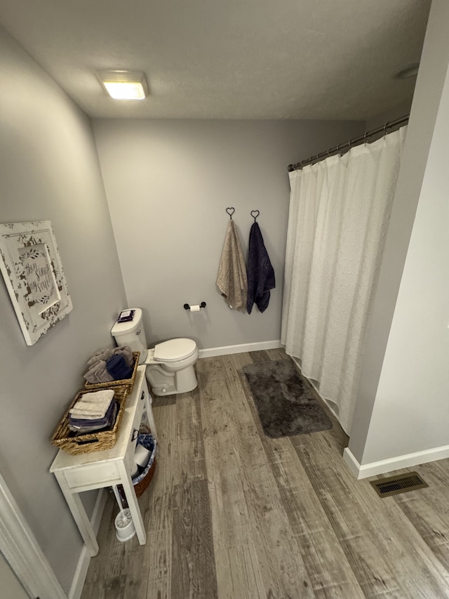 bathroom with wood-type flooring, walk in shower, and toilet