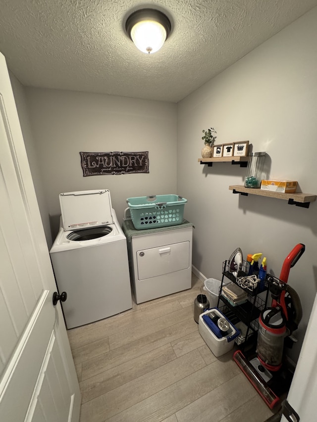 laundry area with light wood-type flooring, a textured ceiling, and washer and dryer