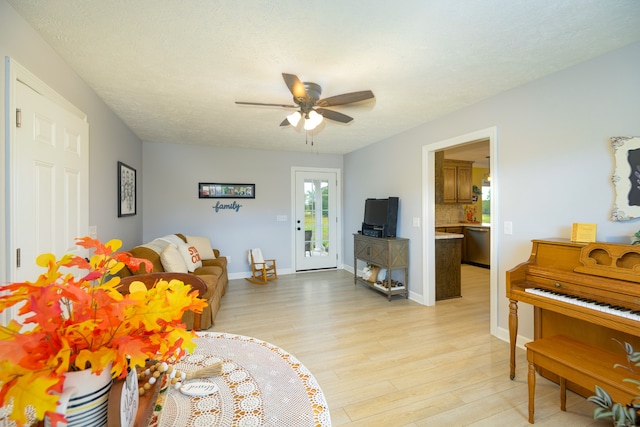 living room with a textured ceiling, ceiling fan, and light hardwood / wood-style flooring