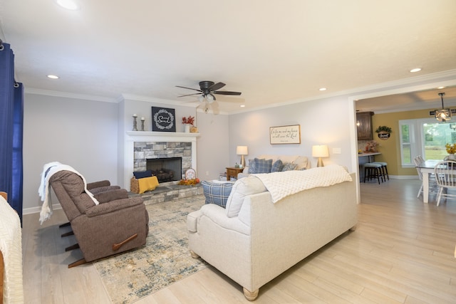 living room featuring light hardwood / wood-style flooring, ceiling fan, ornamental molding, and a stone fireplace