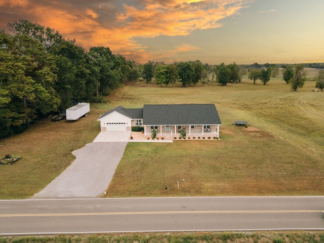 view of front facade with a garage, a yard, covered porch, and a rural view