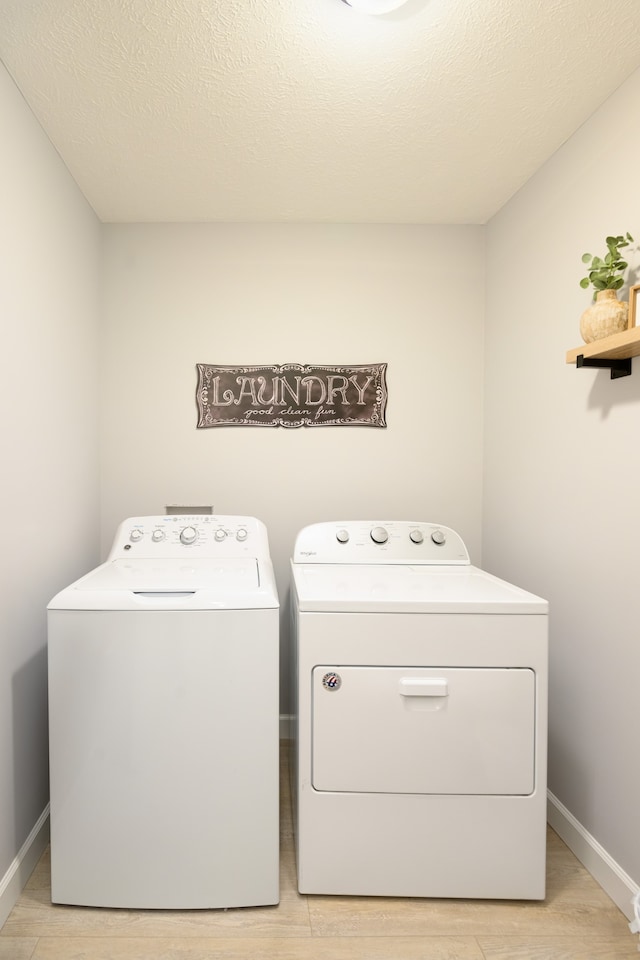 laundry room with washer and clothes dryer, a textured ceiling, and light wood-type flooring