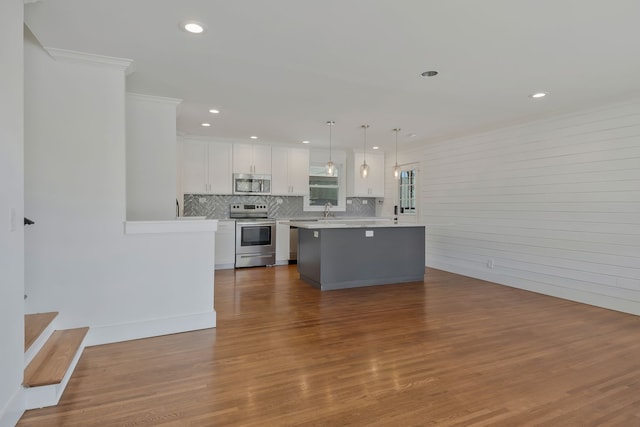 kitchen with hardwood / wood-style floors, appliances with stainless steel finishes, decorative light fixtures, and white cabinets